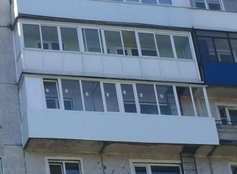 Длинный балкон с обшивкой пластиковыми панелями и остеклением